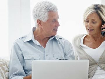 Image of elderly couple using laptop and phone