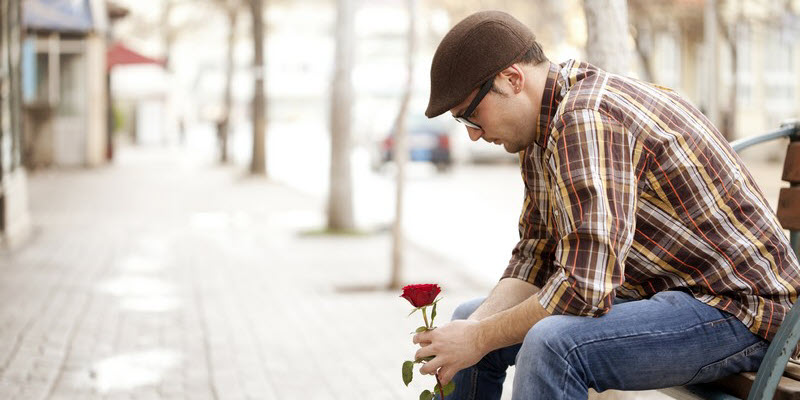 A man looking down on a single rose in his hand