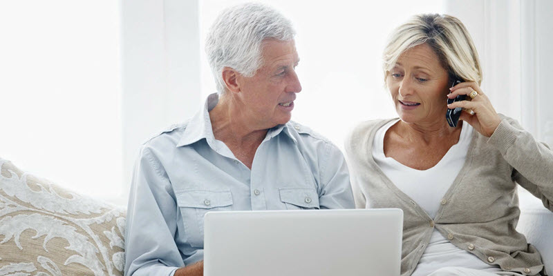 Image of elderly couple using laptop and phone