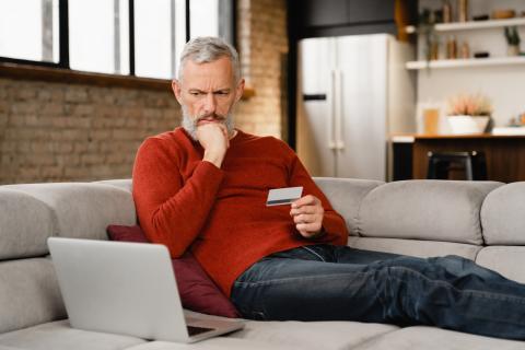 Man sitting on couch holding a credit card and looking at laptop screen